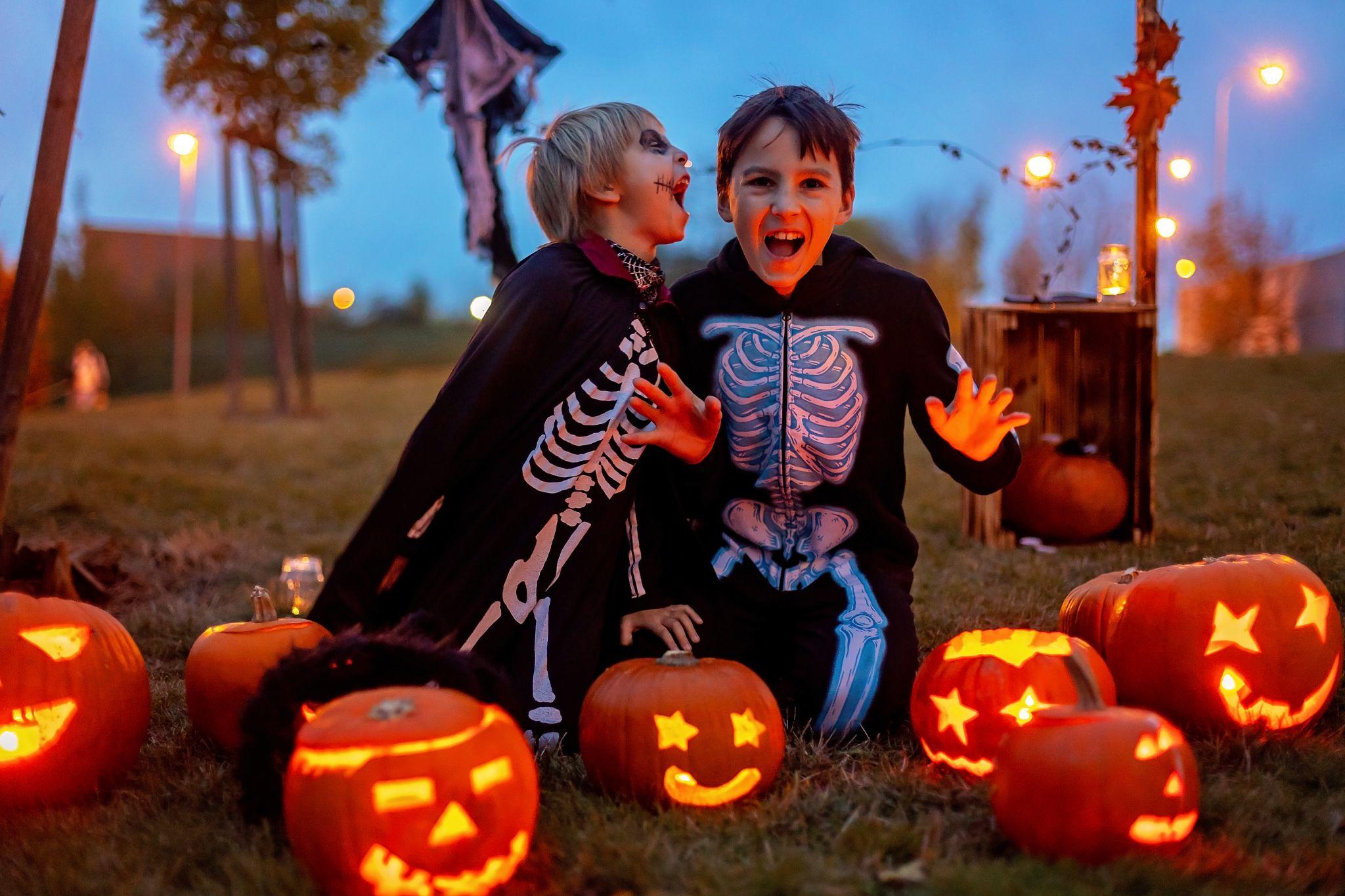 Kids in skeleton costumes sit among glowing pumpkins on Halloween night