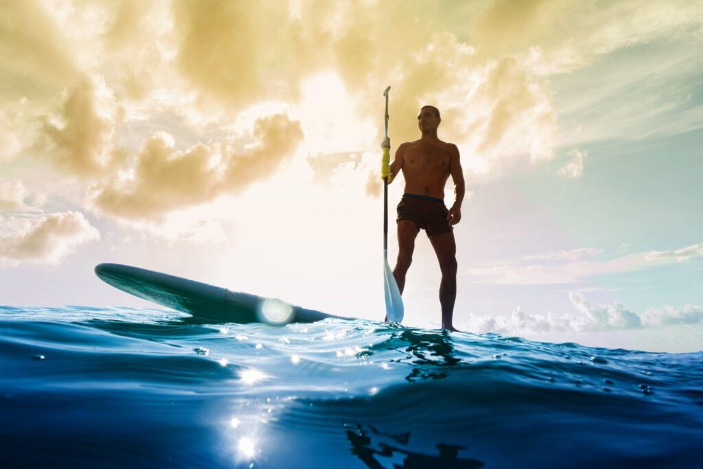 Man paddleboarding on ocean with dramatic sunset sky