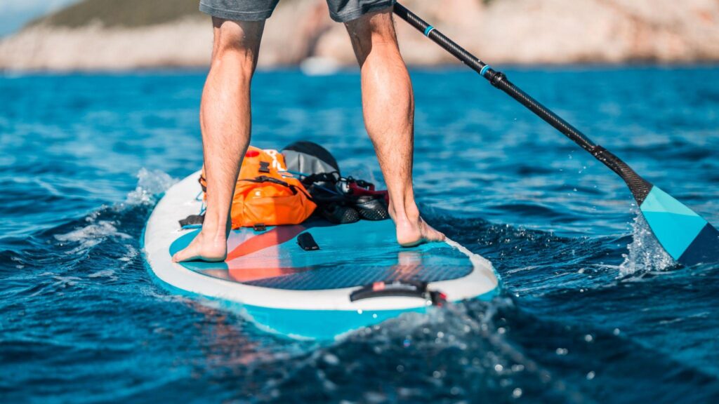 Man paddleboarding with dry bag and equipment on board